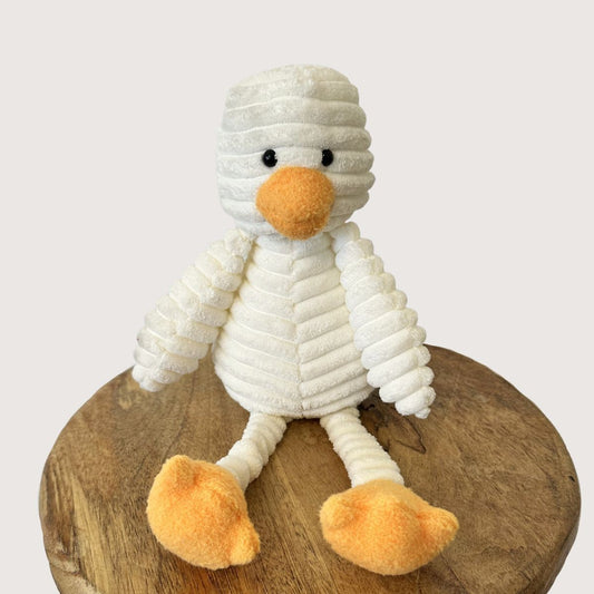White plush duck with orange feet and beak on a wooden surface
