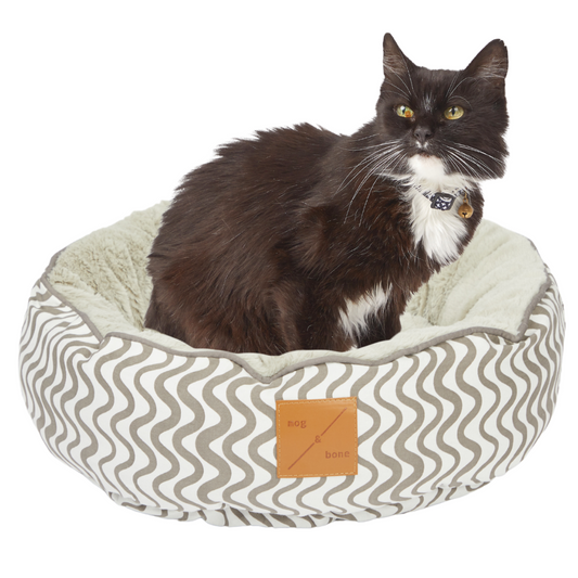 Cat sitting on a patterned pet bed with a visible brand label.