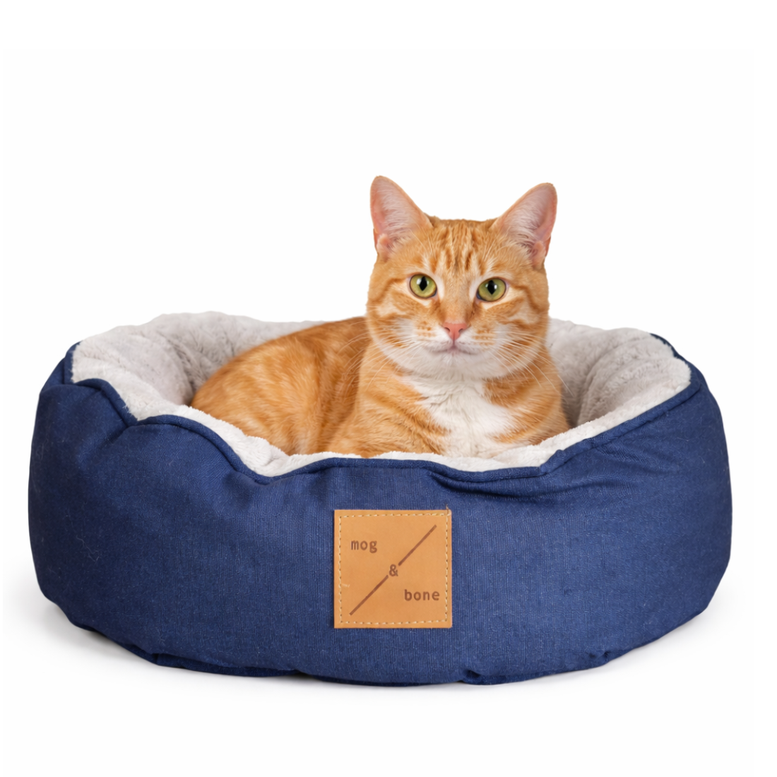 Cat lying in a blue pet bed with a visible brand label on a white background