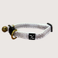 Adjustable hemp cat collar with a jacquard webbing finish and a brass bell fitting, displayed on a wooden surface.