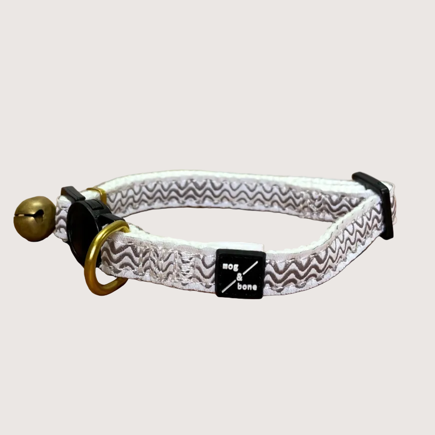 Adjustable hemp cat collar with a jacquard webbing finish and a brass bell fitting, displayed on a wooden surface.