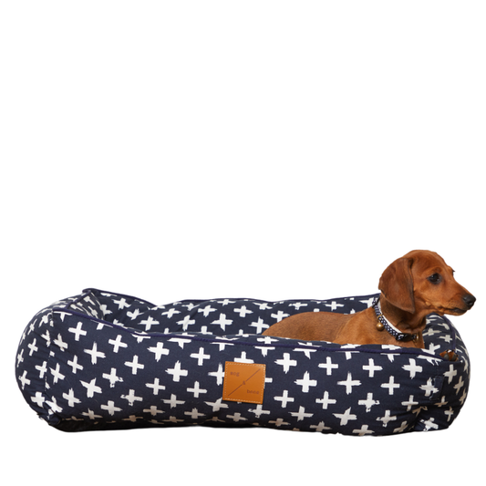 Dog lying on a navy blue and white cross-patterned dog bed with a brown dachshund.