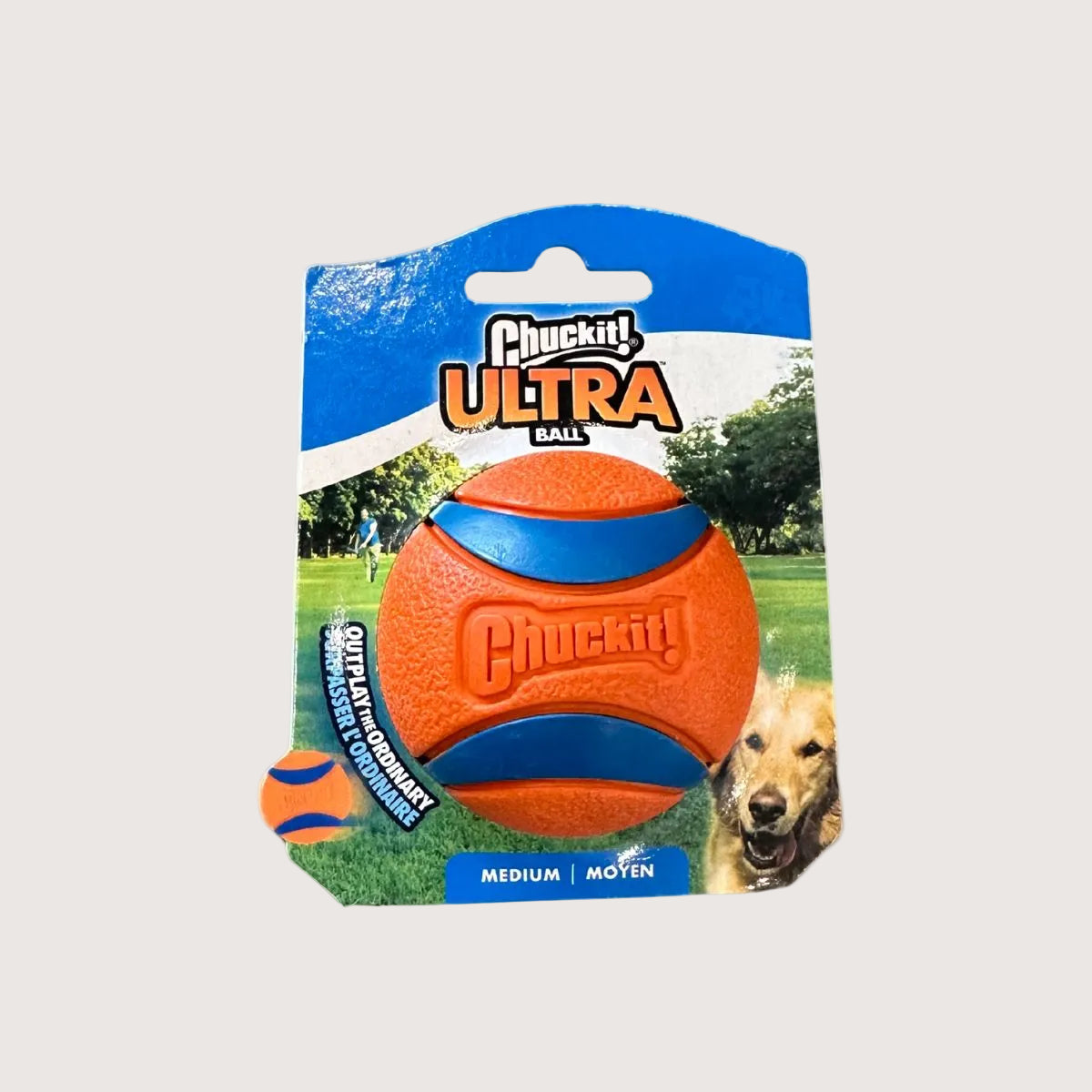 Orange and blue Chuckit! Ultra Ball dog toy in packaging with a dog on a grassy field background.