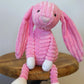 Pink plush bunny sitting on a wooden surface with a plain background