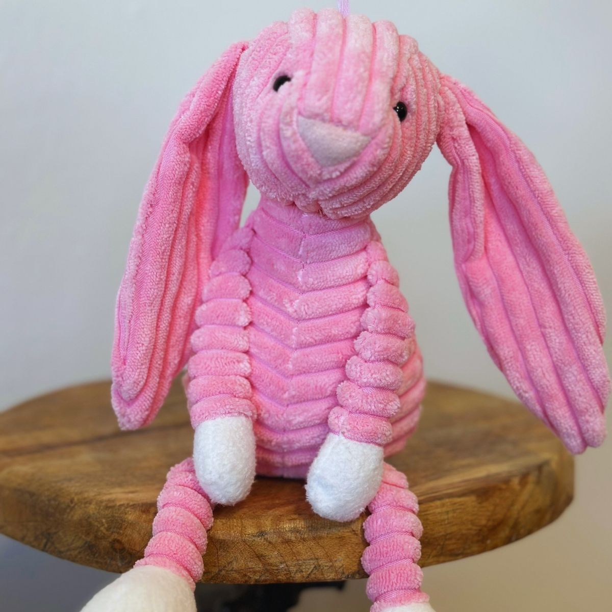 Pink plush bunny sitting on a wooden surface with a plain background