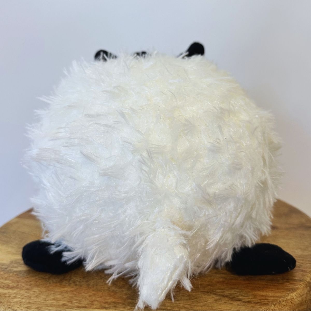 White fluffy dog toy with black feet on a wooden surface