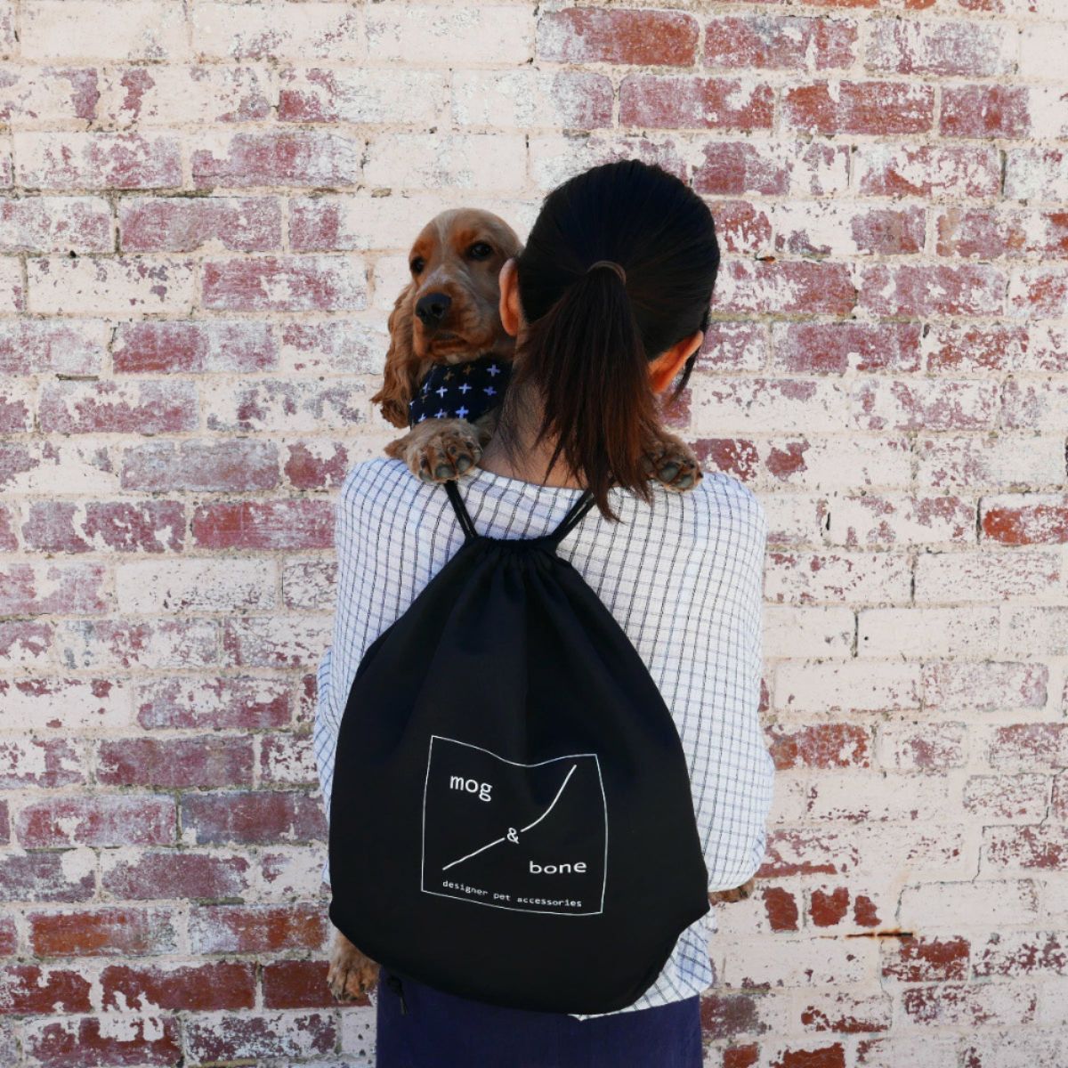 Person holding a dog and a black drawstring bag with 'mag & bone' logo against a brick wall.
