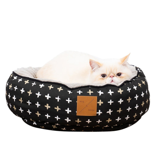 A white cat resting inside a reversible black metallic cross print cat bed.