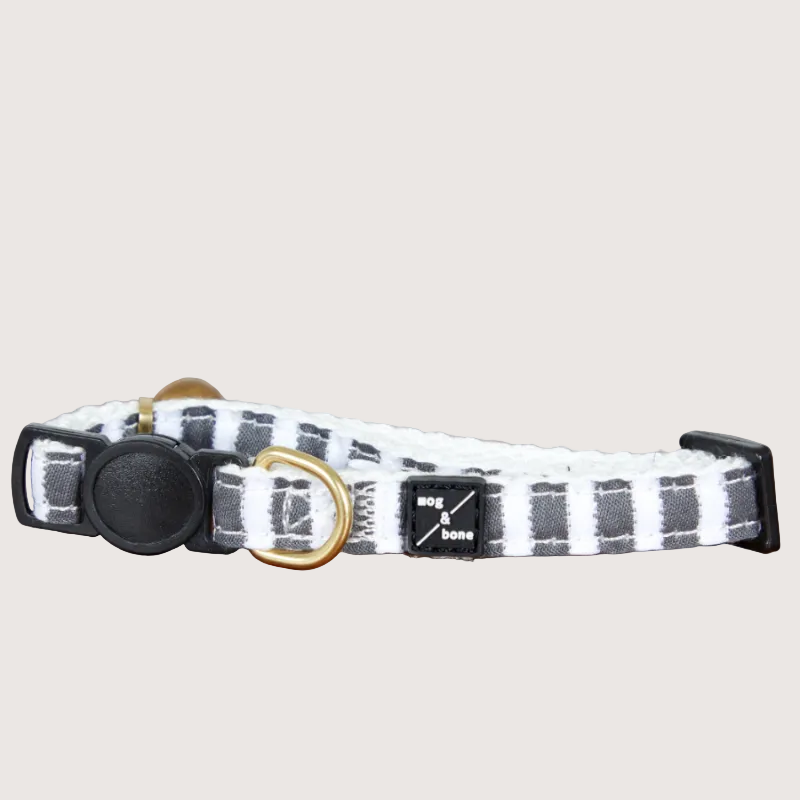 Adjustable hemp cat collar with charcoal gray stripes, a brass bell fitting, and a black buckle.